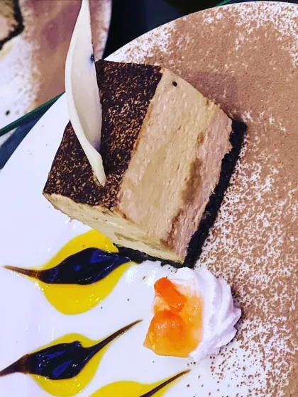 A slice of tiramisu-inspired mousse cake, elegantly dusted with cocoa powder and garnished with white chocolate. I create a wide range of Western and fusion desserts to suit any taste or event theme.