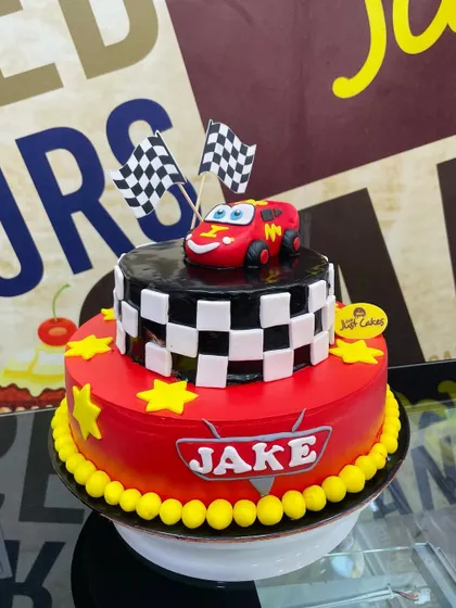A 2.5kg two-tiered cake themed after the movie 'Cars', with a Lightning McQueen topper and checkered flag details.