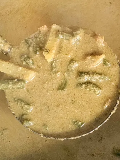 A ladle of creamy vegetable korma, a mild and flavorful curry made with a coconut or cashew base.