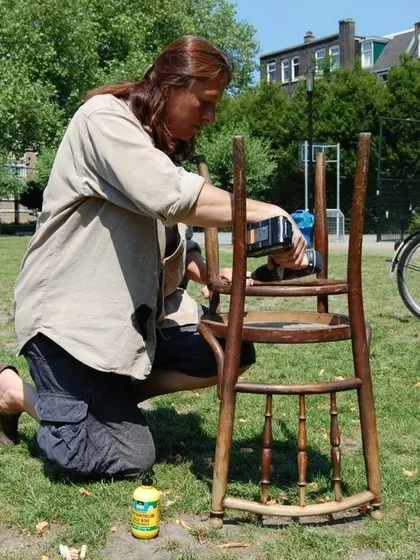 A volunteer repairs a wooden chair outdoors. We often take our workshops to parks and community spaces, combining the joy of fixing with fresh air.
