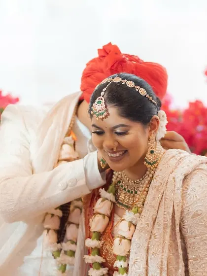 A tender moment during the varmala ceremony, where the groom gently places the garland. The background of pink and red roses adds to the romance of this destination wedding in Thailand.