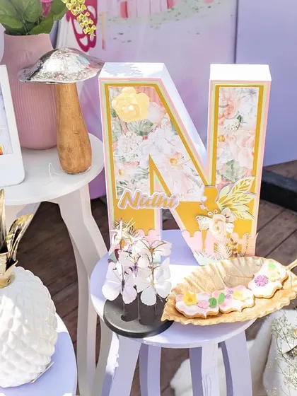 Personalized details for Nidhi's fairy-themed party. The custom initial and framed photos add a warm, personal touch that makes the celebration feel even more special.