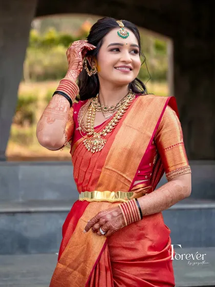 A full-length shot of a bride in her red and gold Kanchipuram saree. The custom blouse and traditional gold jewelry create a perfect bridal look for her Varapooja.