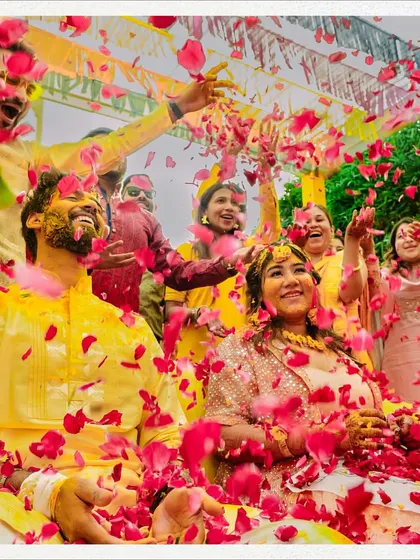 A vibrant and energetic shot of the couple being showered with red rose petals during their haldi, a moment of pure celebration.