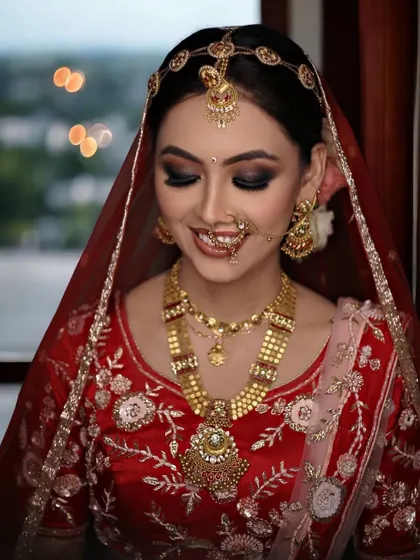 The joy of a bride on her wedding day. This look features dramatic black smokey eyes, a classic updo with a matha patti, and glowing skin for a truly memorable appearance.