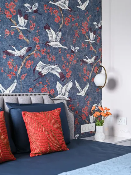 A close-up of the bed and accent wall, showing the textured red cushions that pick up the color from the wallpaper. The hanging pendant light adds a modern touch.