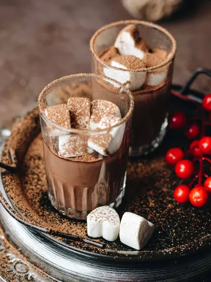 Hot chocolate with marshmallows on a moody, festive tray. The rich brown tones and pops of red from the berries give this a cozy, wintery feel.