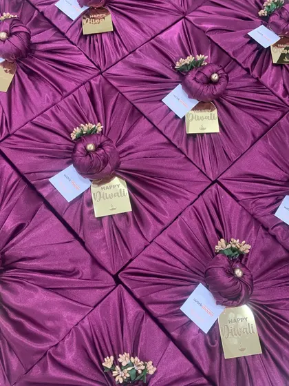 A beautiful array of Diwali gifts wrapped in rich purple satin fabric. The golden 'Happy Diwali' tags add a festive and luxurious finishing touch.