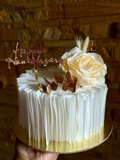 This anniversary cake features delicate wafer paper ruffles and is topped with a single cream rose and gold accents.