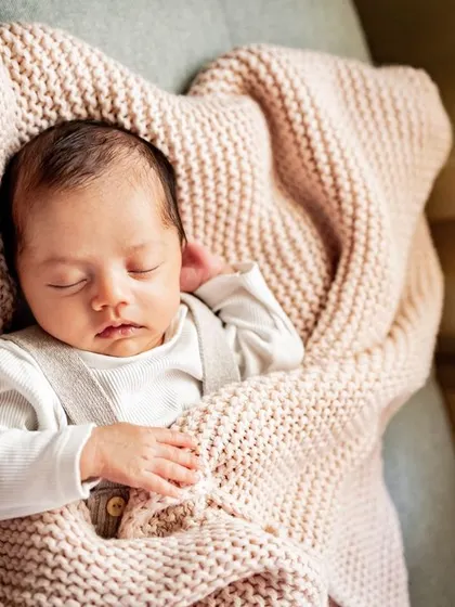 A newborn sleeping peacefully, nestled in a soft pink blanket on the sofa. My at-home sessions mean we can capture these moments wherever your baby is most comfortable.