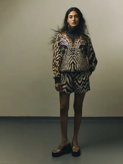 A full-length shot that showcases the complete co-ord set. The simple, industrial-style background allows the bold pattern and the model's strong presence to be the main focus.