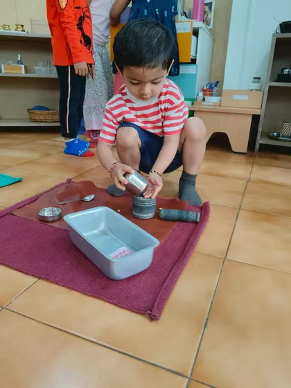 This child is carefully pouring from one container to another. This classic practical life exercise builds concentration, precision, and control of movement.