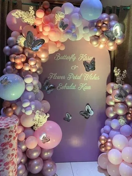 A beautiful butterfly-themed celebration with a custom arched backdrop and a lush balloon garland in shades of pink and purple.