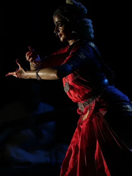 A dramatic, low-lit shot that emphasizes the form and emotion of the dancer. The focus is on the silhouette and the expressive hands.