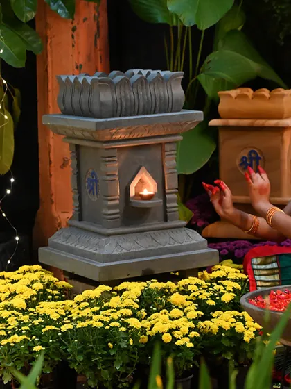 A close-up of our stone Tulasi Brindavan, featuring a lotus-carved top and a niche for a diya. Surrounded by yellow chrysanthemums, it is a beautiful addition to any festive decor.