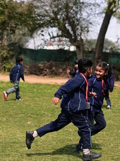 Two students from HDFC School running and playing freely on the grass during their farm visit.