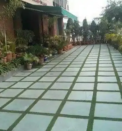 A large patio or driveway paved with square-cut stones and synthetic turf in the gaps. This is a low-maintenance alternative to natural grass for a clean, geometric look.