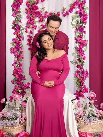 A full-length view of our floral setup. The expecting couple shares a happy moment, seated amidst a cascade of pink and purple flowers, creating a lush and romantic scene for their maternity photos.