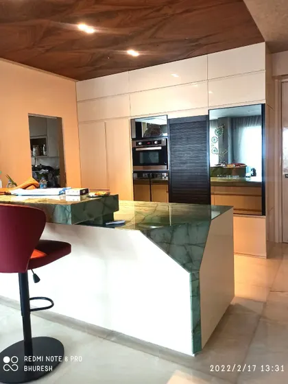An island kitchen designed for the Jhamdar residence, featuring a stunning green marble countertop. The island serves as both a workspace and a casual dining spot with a comfortable bar stool.