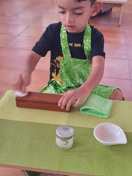 A child polishes a wooden box. This activity not only cares for the environment but also involves a multi-step process that builds concentration and a sense of order.