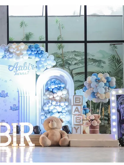 The main stage for the blue teddy bear party. The setup includes a custom backdrop, cascading balloon installations, illuminated "BABY" blocks, and a large teddy bear prop.