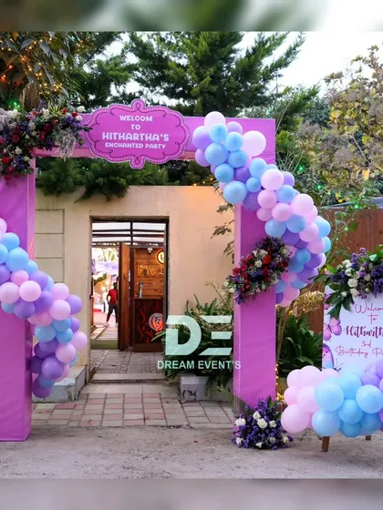 A grand entrance arch for an 'Enchanted Party', decorated with a pastel balloon garland and a custom welcome sign.