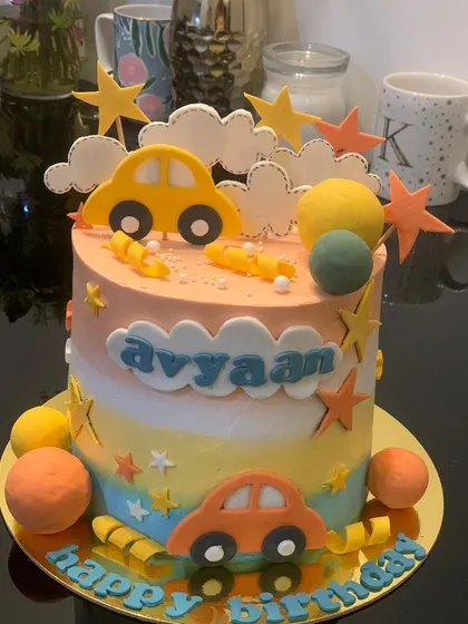 A colorful car cake with a sunset-inspired ombre effect. The design is decorated with fondant cars, clouds, and stars.