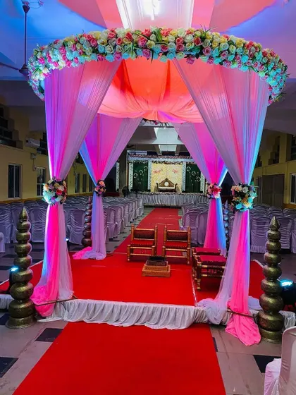 A breathtaking view down the aisle towards the wedding mandap. The entrance is framed by a canopy of pink and white drapes and flowers, creating a grand and romantic pathway for the ceremony.