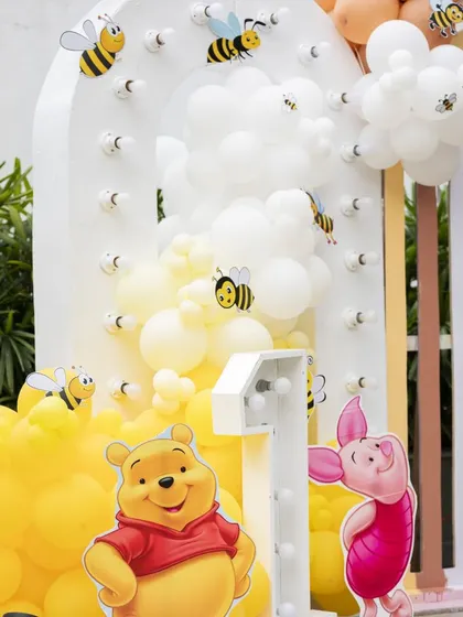 A 'Winnie the Pooh' themed backdrop with a light-up '1' and bee details. The yellow and white balloons mimic a beehive, adding a creative touch to the setup.