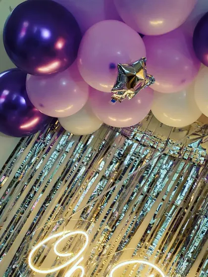 A close-up of the top of the balloon arch, showing the mix of chrome purple, pastel purple, and white balloons.