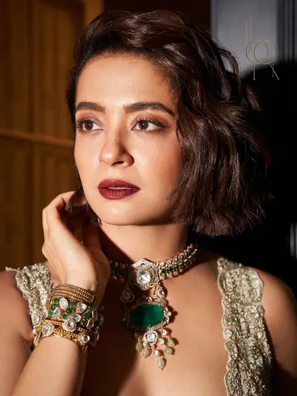 A close-up of Surveen Chawla, showcasing the intricate details of her emerald necklace and matching stacked bracelets.