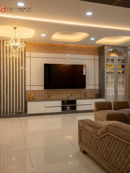 An intricate and luxurious living room design where the TV unit is flanked by fluted panels and a CNC-cut jali partition for the pooja area. The layered false ceiling adds to the grandeur of the space.