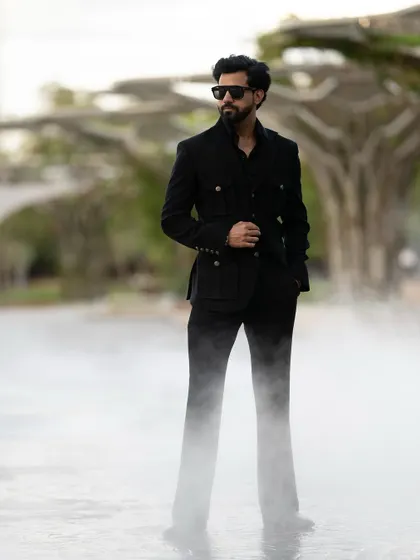 The dramatic, misty setting adds an element of mystery and intrigue, perfectly complementing the all-black, sophisticated ensemble.