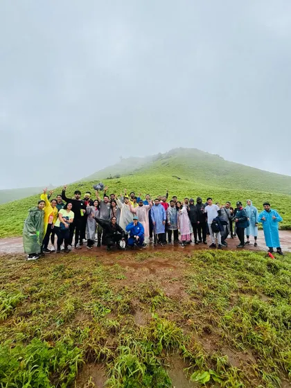 A wide shot of a large group on a green hill, celebrating their trek.