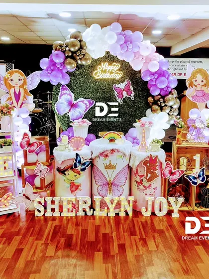 A whimsical fairy and butterfly theme for Sherlyn Joy's first birthday. I combined a green hedge backdrop with a purple balloon arch, fairy cutouts, and marquee letters to create this magical garden party look.