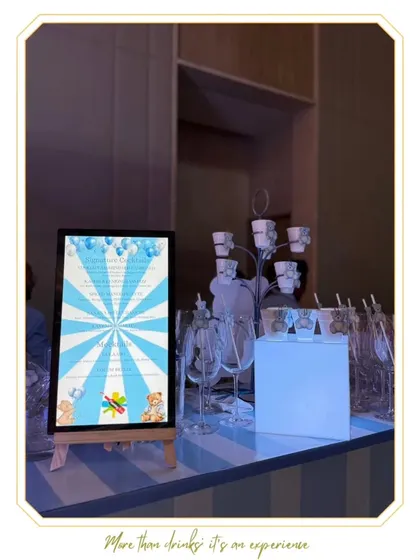 A themed bar setup for a cradle ceremony, featuring a custom menu board with a blue and white striped design and teddy bear graphics to match the event's theme.