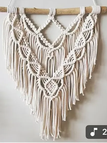 A beautiful, handcrafted macrame piece with layered patterns and a gentle V-shape. It's made from natural cotton cord and hung on a simple wooden dowel.
