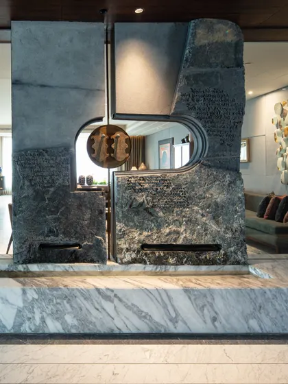 A home's entrance should be an evocative experience. We designed this majestic water feature from massive, naturally split stone slabs, etched with Pali script and adorned with brass 'Khadau' sandals to create a serene and symbolic threshold that offers blessings upon entry.