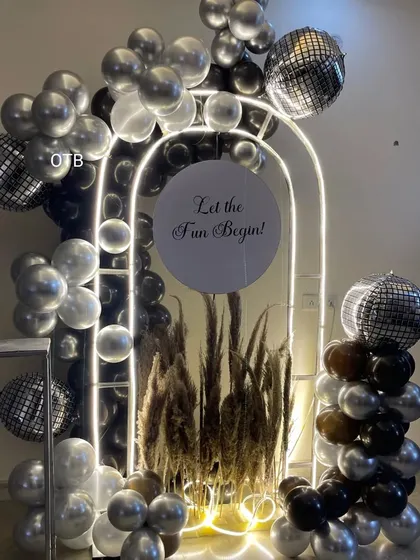 A modern and moody party theme. This setup features a lit arch with black and silver balloons, pampas grass, and disco balls for a unique and stylish look.