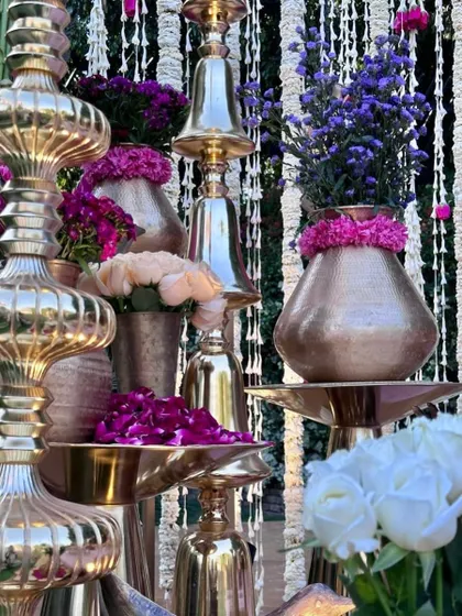 The fine details of our vedi decor, featuring stacked brass bells, hammered-metal vases, and a mix of purple and peach florals.