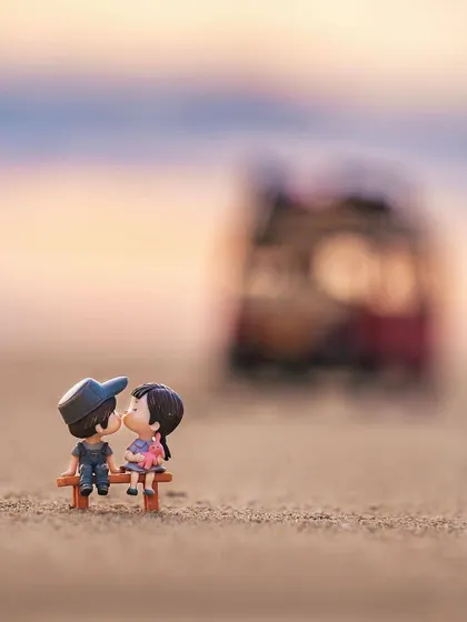 A miniature couple shares a kiss on a bench, with the toy bus from the previous shot blurred in the background. This series tells a sweet, romantic story using miniatures.