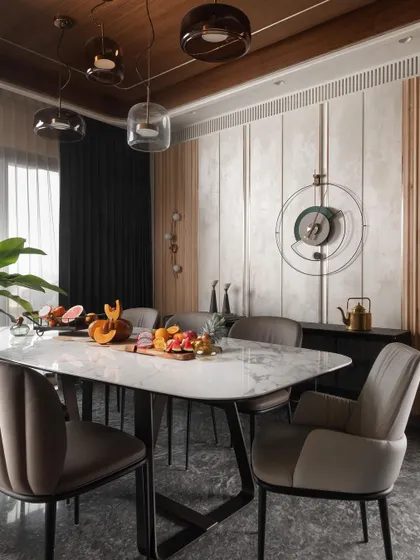 The dining area is defined by a curved ceiling detail and a sophisticated mix of materials. A marble-topped table is surrounded by comfortable upholstered chairs, set against a backdrop of textured wall panels and wood fluting.