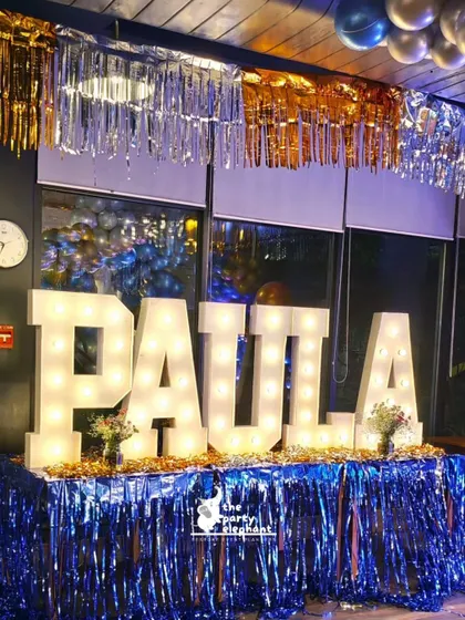 Large marquee letters spelling out the birthday girl's name served as a bold and bright centerpiece for the party decor, placed on a table with a shimmering blue fringe skirt.
