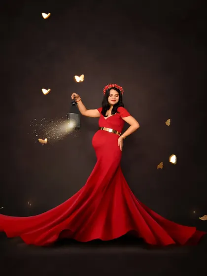 A striking solo portrait in a vibrant red gown. The mom-to-be holds a lantern with sparkling effects, creating a magical and captivating image against a dark background.