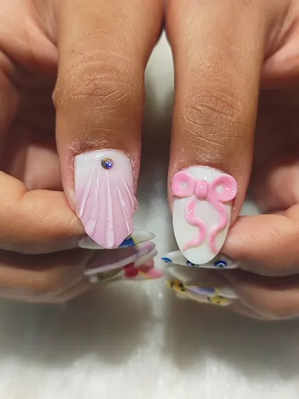 A close-up of the thumb nails from the mismatched set, featuring a 3D seashell texture and a cute pink 3D bow.