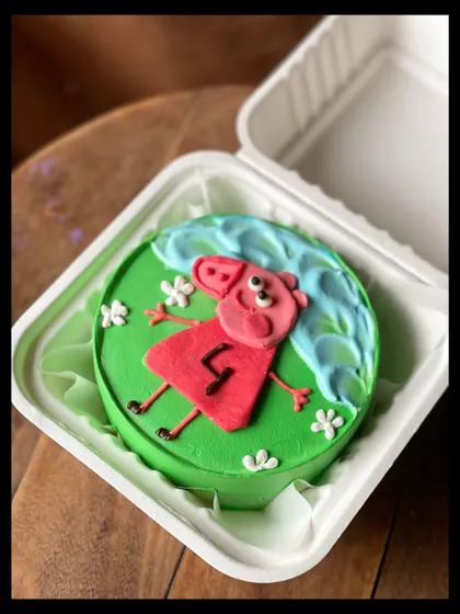 A fun and colorful Peppa Pig bento cake for a 4th birthday. Peppa is shown lying in the grass next to a puddle, just like in the show.