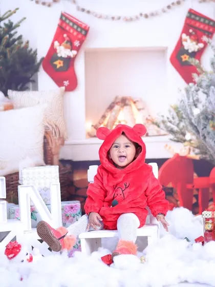 A cozy Christmas scene with a baby in a cute red hooded jacket, sitting among presents and festive decorations.