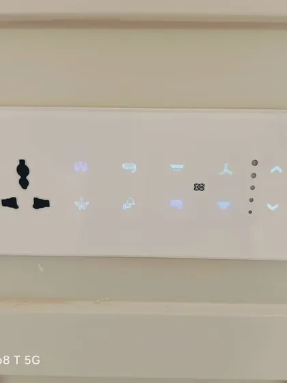 A close-up of our white glass smart touch panel, seamlessly integrated into a neutral wall. The illuminated icons indicate controls for various lights, a fan with 5-speed regulation, and scene settings.