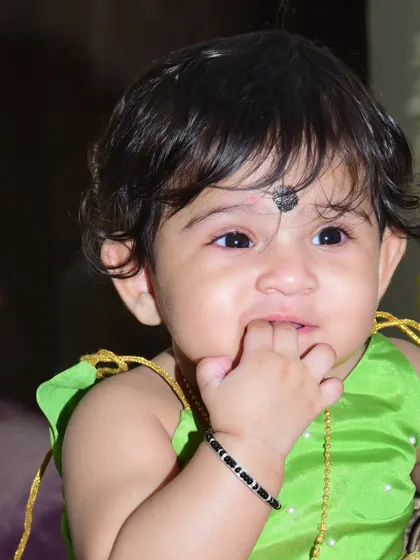 A close-up of a baby in a bright green top, caught in a thoughtful moment with a finger near their mouth. These unposed, natural shots are often the most cherished.