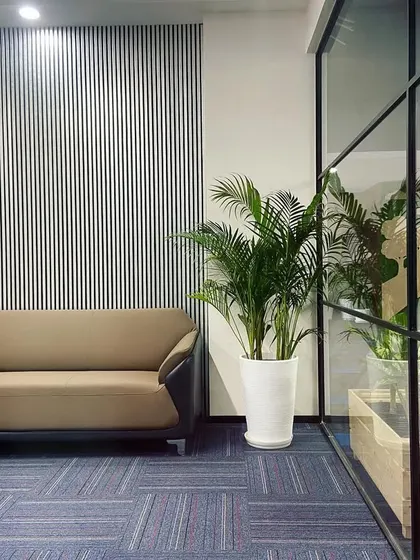 A modern brown sofa and a tall Areca Palm are set against a contemporary fluted wall panel. The combination of textures and natural elements creates a sophisticated and calming corner.